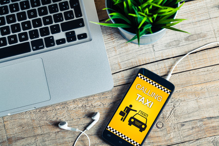 Calling taxi app on a mobile phone screen. Wooden desk office. Workplace.の写真素材