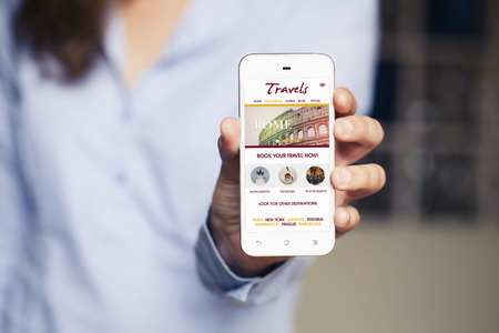 Travel website template design in a mobile phone. Woman holding smart phone in the hand.の写真素材