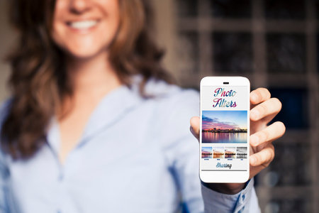 Smiling woman holding a mobile phone with photo filters app on the screen. Generic app template...