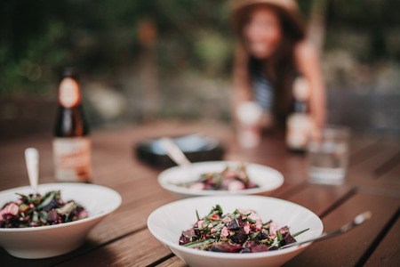 Three dishes of salad in a table, with a girl in the background.の写真素材