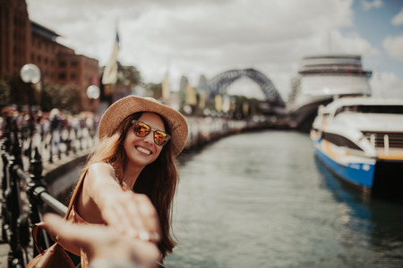 Woman in sunglasses holding boyfriend hand, while taking a photo of her, in Sydney Harbour.の写真素材