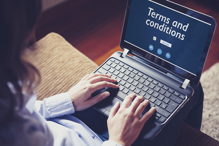 Woman reading Terms and conditions in a laptop while sitting on a sofa at home.の写真素材