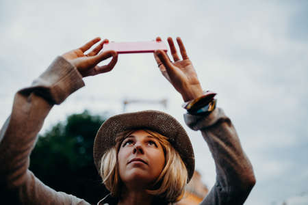 Cute woman with a hat taking a picture with a mobile phone in the street.の写真素材