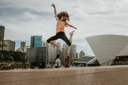 SYDNEY, AUSTRALIA - FEBRUARY 26, 2017: Happy woman jumping in the air with the Sydney Harbor in the background, and Opera House in the right part.のeditorial素材