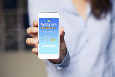 Woman hand holding a mobile phone with weather information in the screen.の写真素材