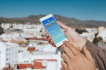 Hand holding a cellphone with weather information in the screen.の写真素材