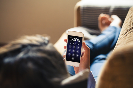 Woman at home holding a mobile phone with passcode in the screen. Unlocking phone concept.の写真素材