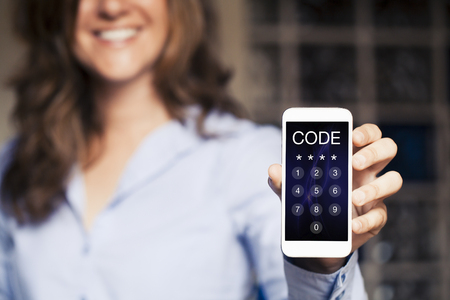 Smiling woman holding a mobile phone with passcode in the screen. Unlocking device.の写真素材