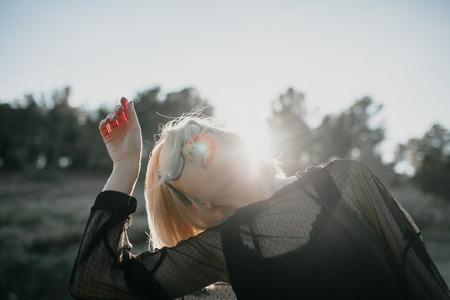 Cute blonde woman posing in profile with sunglasses and black clothes with sun backlighting, in nature. Copy space above.の写真素材