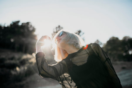 Conceptual portrait of cute blonde woman posing in profile with sunglasses and black clothes with...