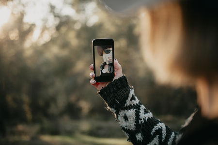 Woman taking a photo with a mobile phone in nature. She appears in the screen through the device frontal camera.の写真素材