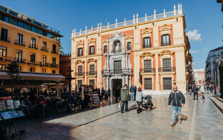 MALAGA, SPAIN - DECEMBER 5th, 2017: Episcopal palace facade and tourist sitting on the restaurants terraces and walking around Bishop Square in Malaga city center, on December 5th, 2017.のeditorial素材