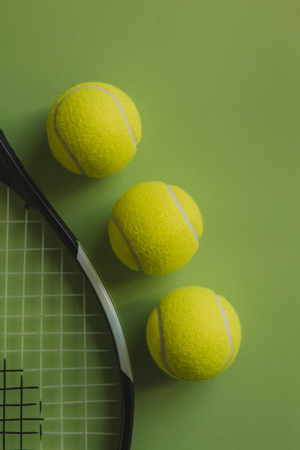 Three tennis balls and a tennis racket on green background.の写真素材