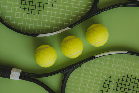 Three tennis balls and two tennis rackets on green background.の写真素材