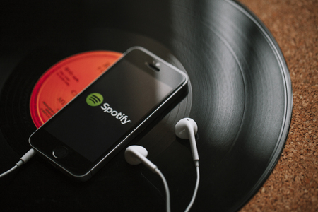 MALAGA, SPAIN - MARCH 5, 2018: Mobile phone with Spotify Music service in the screen and white earphones on a black vinyl record.のeditorial素材
