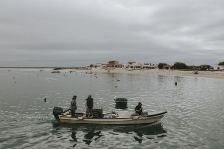 Armona Island, Portugal - March 23, 2018: Three men arriving to Armona Island pier in a little boat in a cloudy day in Olhao, Portugal.のeditorial素材