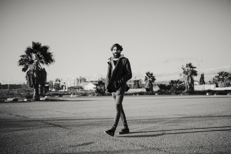 Black and white portrait of young man walking outdoors at sunset with urban clothes style.の写真素材