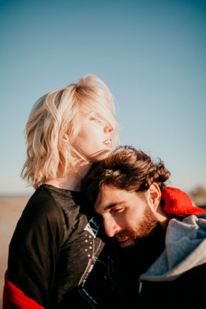 Blonde woman and bearded man embracing at sunset romantically.