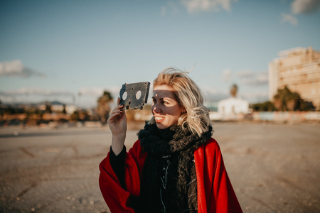 Blonde alternative woman playing with a VHS tape outdoors at sunset. Creative filmmaker concept.の写真素材