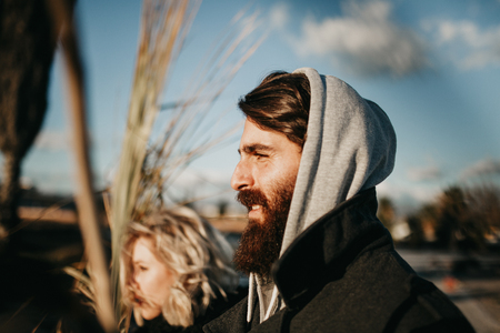Young bearded man posing outdoors close to his girlfriend. Cool and weird young couple posing outdoors while holding palm tree branches.の写真素材