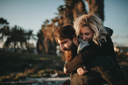 Blonde woman holding in her boyfriend back while they enjoy a date together at sunset.の写真素材
