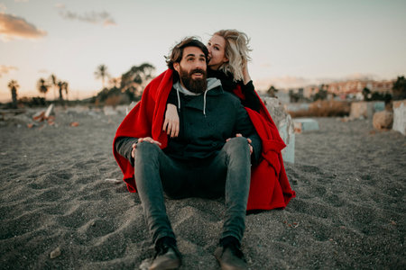 Young hipster couple sitting on the beach sand embraced romantically.の写真素材