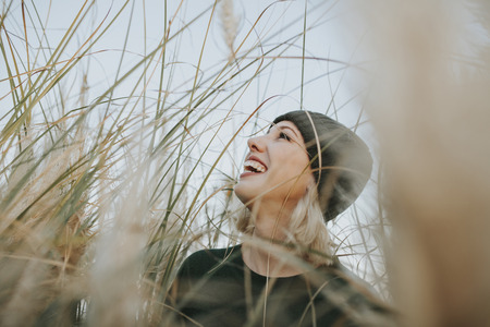 Happy blonde woman with a knit hat on surrounded of reed plants in nature.の写真素材