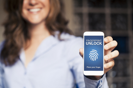 Smiling woman holding a mobile phone with Fingerprint Unlock notification in the screen.の写真素材