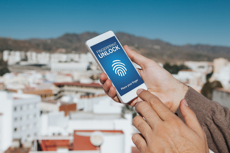 Man holding a mobile phone in the hand with Fingerprint Unlock system in the screen.の写真素材