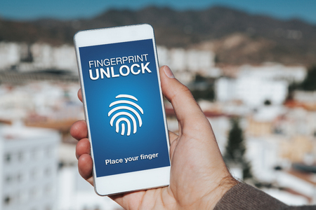 Fingerprint Unlock notification in a mobile phone screen. Man hand holding phone with city background.の写真素材