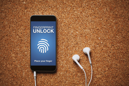 Mobile phone with Fingerprint Unlock system in the screen, white earphones, and copy space.の写真素材