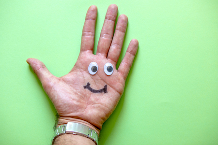 Happy face made with plastic eyes and drawn smile on a human hand palm, with green background.の写真素材