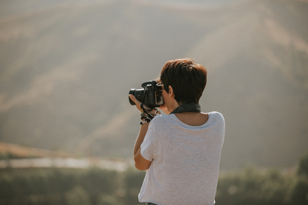 Woman in t-shirt taking a photo with a camera in nature with daylight.の写真素材