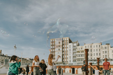 BRIGHTON, ENGLAND - October 24th, 2018: Kids playing in the beach while a man creates big soap...