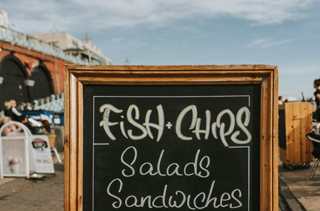 Blackboard with restaurant menus and information in the middle of a promenade, with Fish and Chips, salads, sandwiches and other food.の写真素材