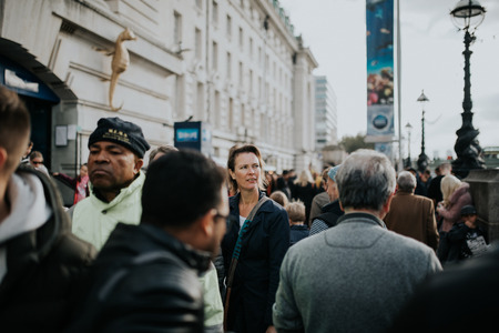 LONDON, ENGLAND - 25th October, 2018: Woman walking inside the crowd across The Queen's Walk, in a sunny day in London, Uk.のeditorial素材