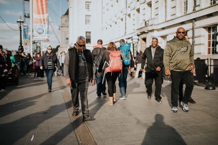 LONDON, ENGLAND - 25th October, 2018: Men walking inside the crowd across The Queen's Walk, in a sunny day in London, Uk.のeditorial素材