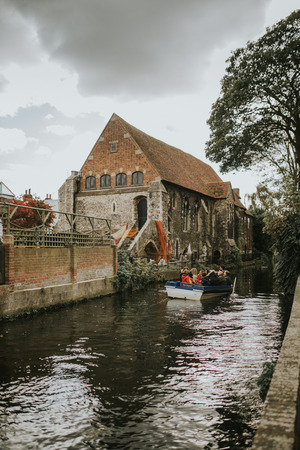 CANTERBURY, ENGLAND - October 28th, 2018: People enjoying a touristic travel in a little boat along Stour River, with a Church in the background, in Canterbury, England.のeditorial素材