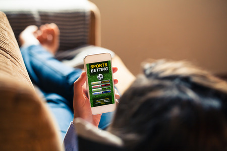 Woman holding a mobile phone with sports betting website app in the screen, while lying down at home at home.の写真素材