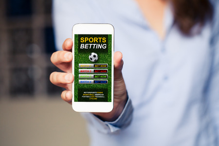Sports betting website in a mobile phone screen while woman holds the device.の写真素材