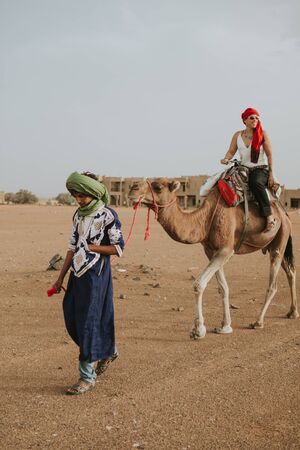 Sahara Desert, Morocco - September 18th, 2019: A berber man guiding a caravan of camels with tourists to the desert dunes, during adventure experience in Sahara Desert, Morocco .のeditorial素材