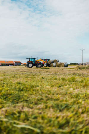 Red tractor loading a trailer with straw bales during harvesting timeの写真素材