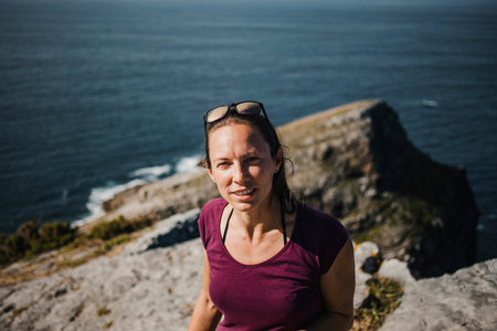 Cute white woman standing in a cliff with the sea in the background.