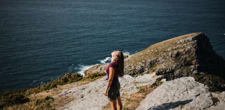 Woman standing at the coastline on the top of a cliff, with sea in the background.の写真素材