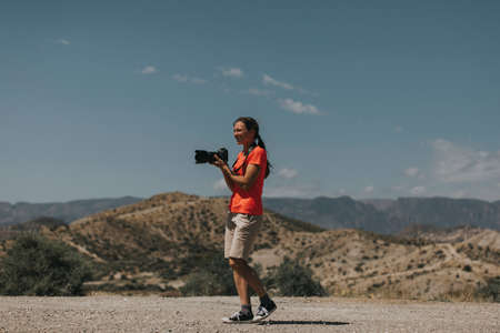 Sports woman photographer taking photos in Tabernas Desert, Spain, in a sunny day, with an orange color t-shirt.の写真素材