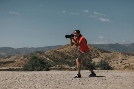 Sports woman photographer taking photos in Tabernas Desert, Spain, in a sunny day, with an orange color t-shirt.の写真素材