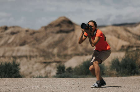 Sports woman photographer taking photos in Tabernas Desert, Spain, in a sunny day, with an orange color t-shirt.の写真素材