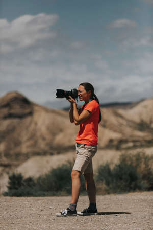 Sports woman photographer taking photos in Tabernas Desert, Spain, in a sunny day, with an orange color t-shirt.の写真素材