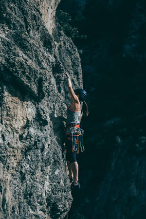 Woman climbing a rock with a lot of climbing gear hanging from her harnessの写真素材