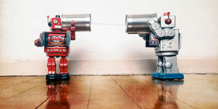 tow retro robots talk on tin can phones on an old wooden floor with reflectionの写真素材